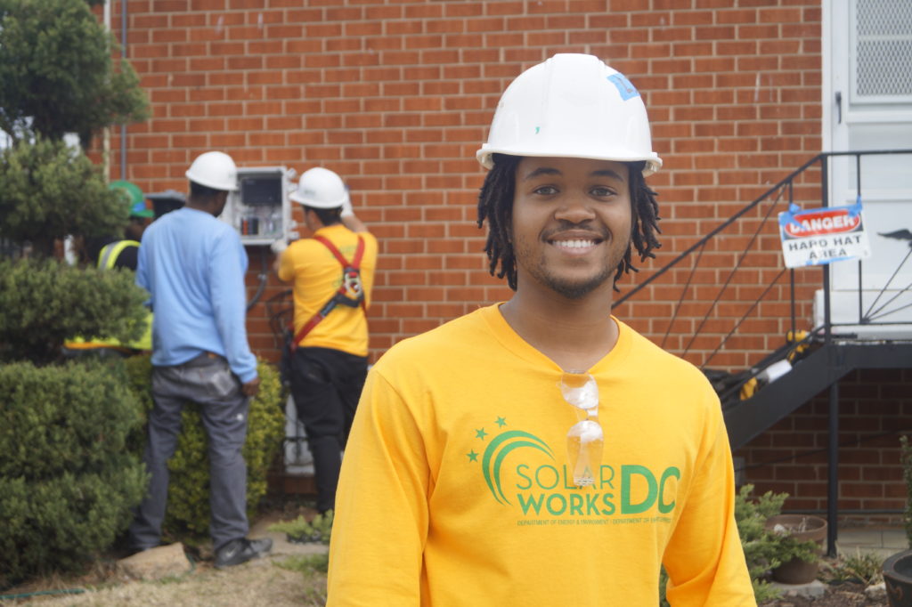 SolarWorks DC job trainee smiles as other participants work onsite. 