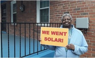 Anna Butler smiles with a sign that reads "We went solar!"